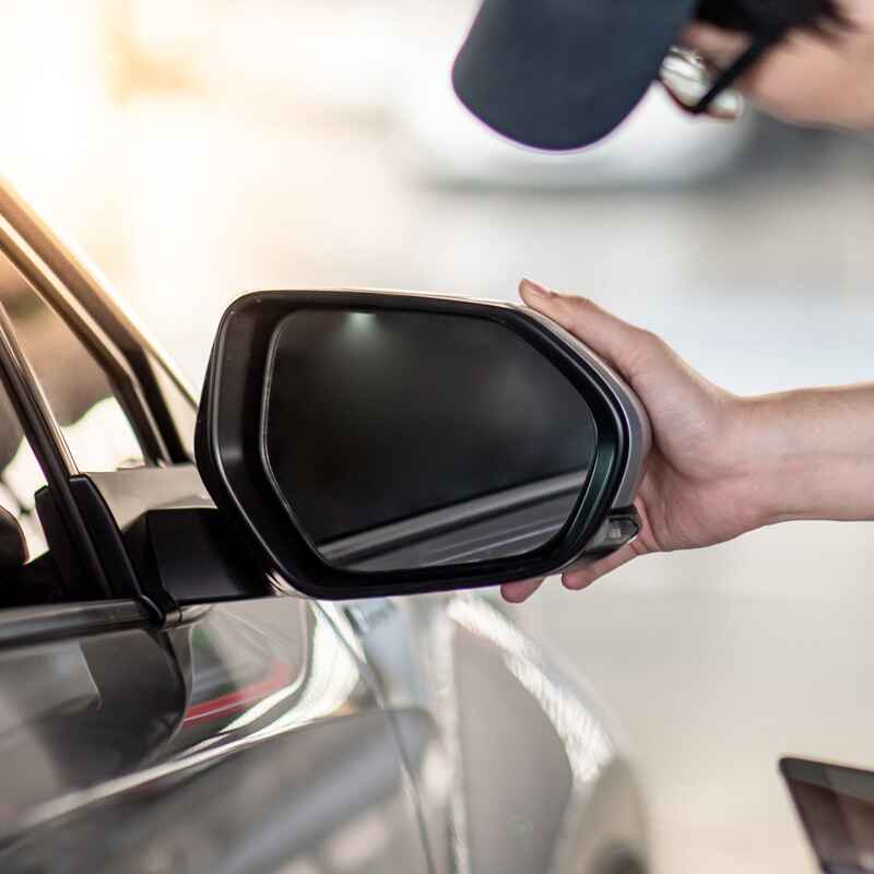 A person inspects a car's side mirror, representing Excellence Auto Glass services in Burnaby, BC.